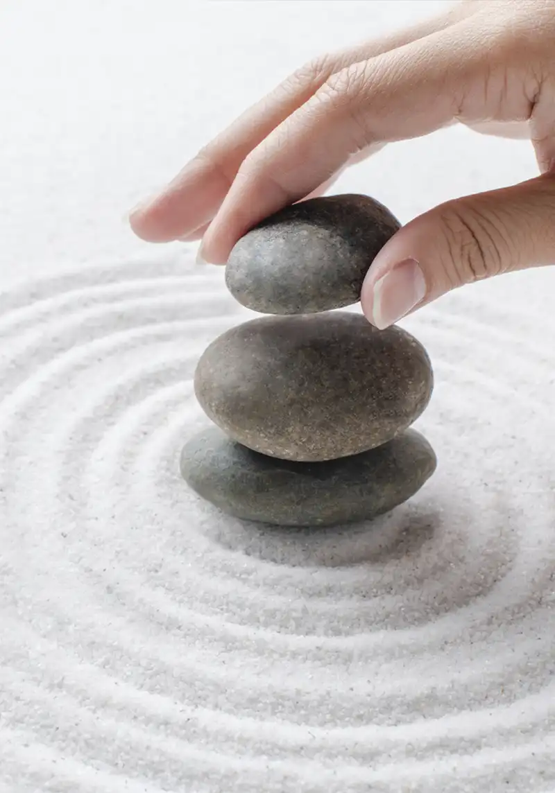 Main posant un galet sur une pile de pierres zen dans le sable